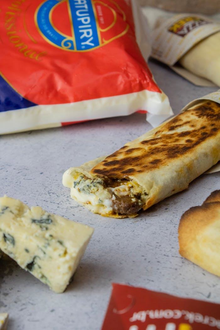 Close-up of a grilled doner roll surrounded by cheese and packaged ingredients.