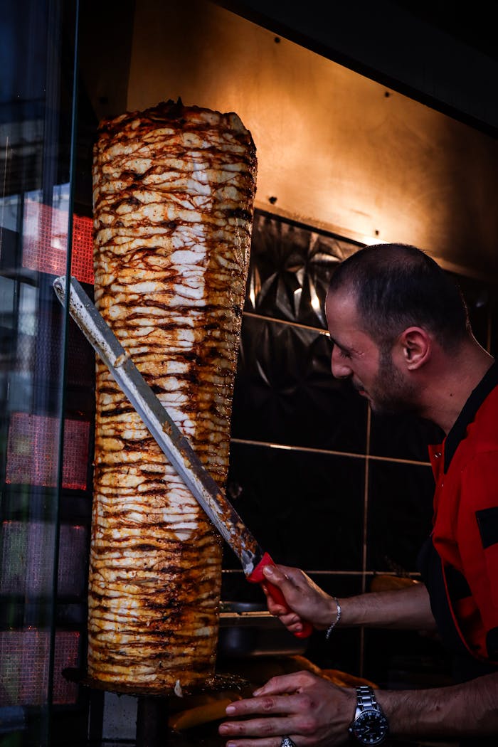 A chef slices a large doner kebab with precision in a kitchen, showcasing culinary skills.